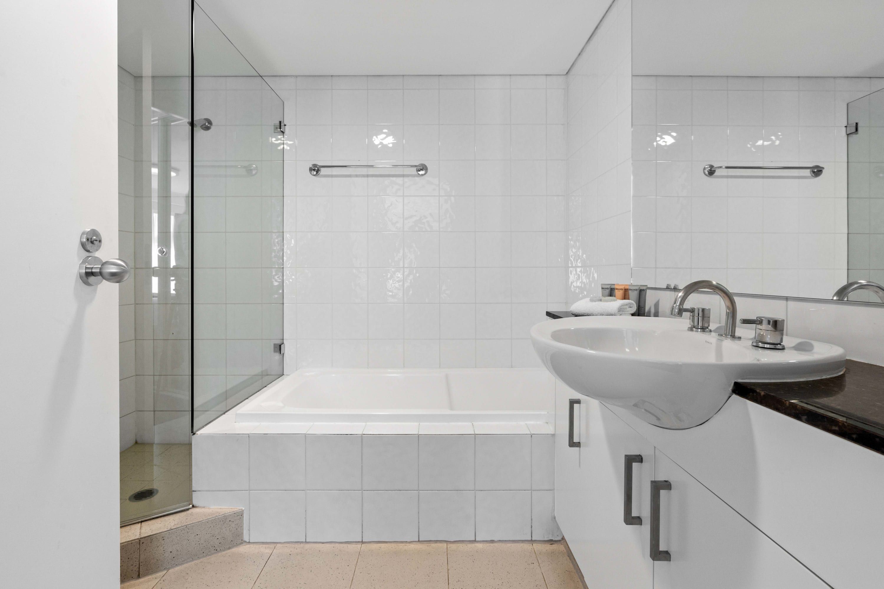 A modern bathroom with a glass shower enclosure, a white bathtub, and a sink with a countertop.