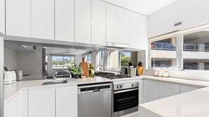 A modern kitchen with white cabinets, a dishwasher, an oven, and a window with a city view. - Sydney Harbourside Apartment (Sydney)
