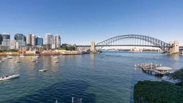 A waterfront cityscape with a prominent bridge, multiple boats, and high-rise buildings.