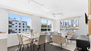 A modern living room with a dining area, large windows, and a view of the city. - Sydney Harbourside Apartment (Sydney)
