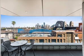 A balcony with a table and chairs, overlooking a cityscape with a bridge and buildings. - Dream Views of Sydney CBD (Sydney)