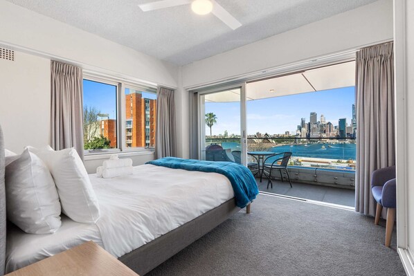 A hotel room with a large bed, a balcony with a city view, and a table with chairs. - Dream Views of Sydney CBD (Sydney)