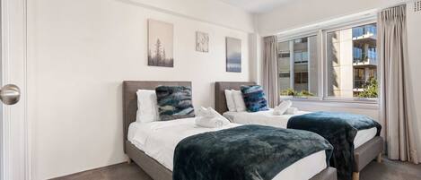 A hotel room with two beds, a large window, and artwork on the wall.