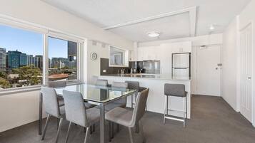 A modern kitchen with white cabinets, a stainless steel refrigerator, and a window overlooking a cityscape.