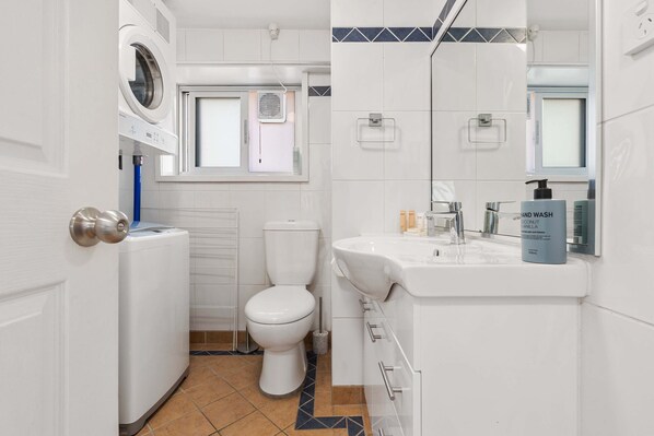 A modern bathroom with a built-in washing machine, toilet, and sink. - Dream Views of Sydney CBD (Sydney)