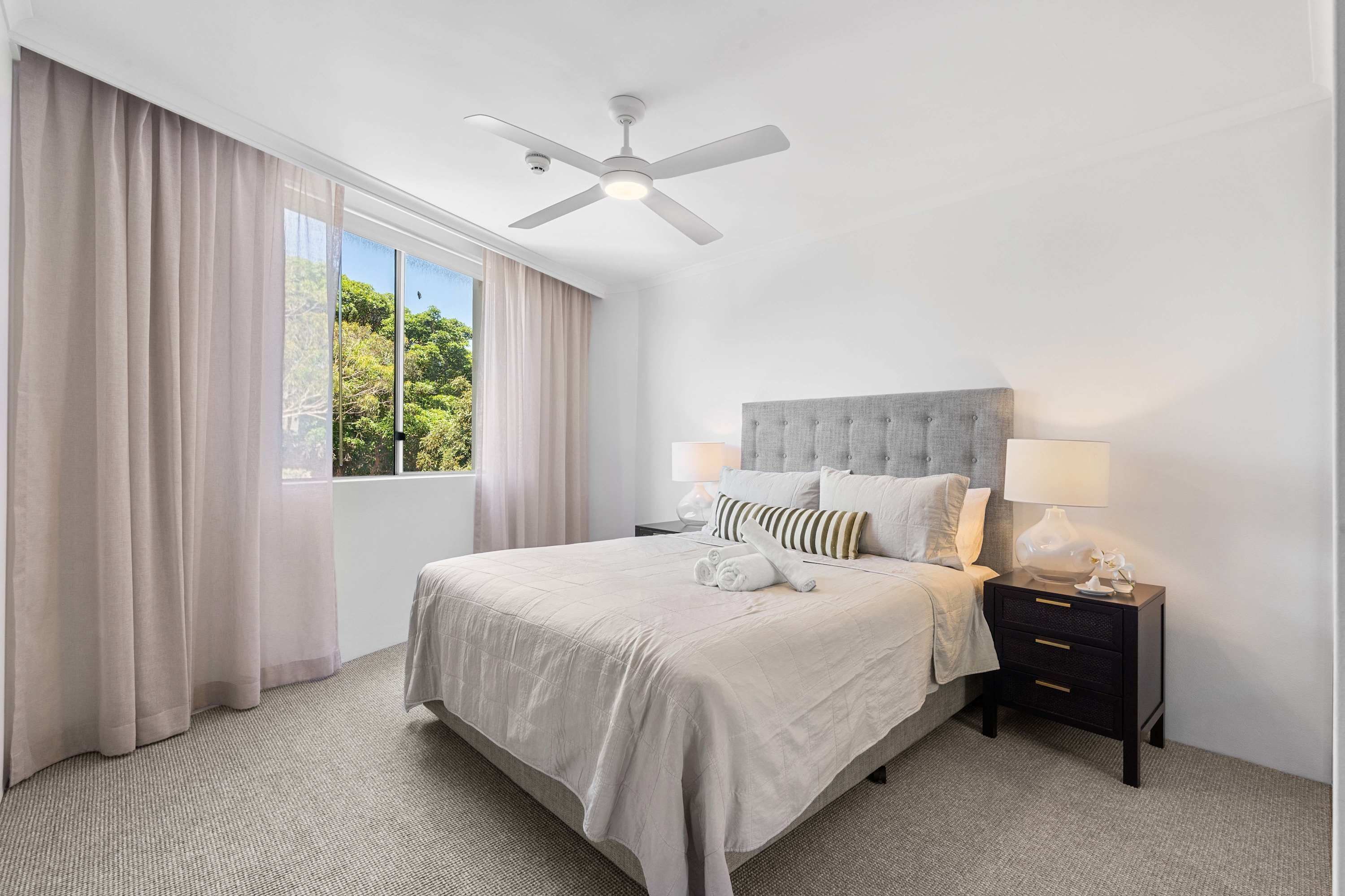 A neatly arranged bedroom with a bed, bedside tables, and a ceiling fan.