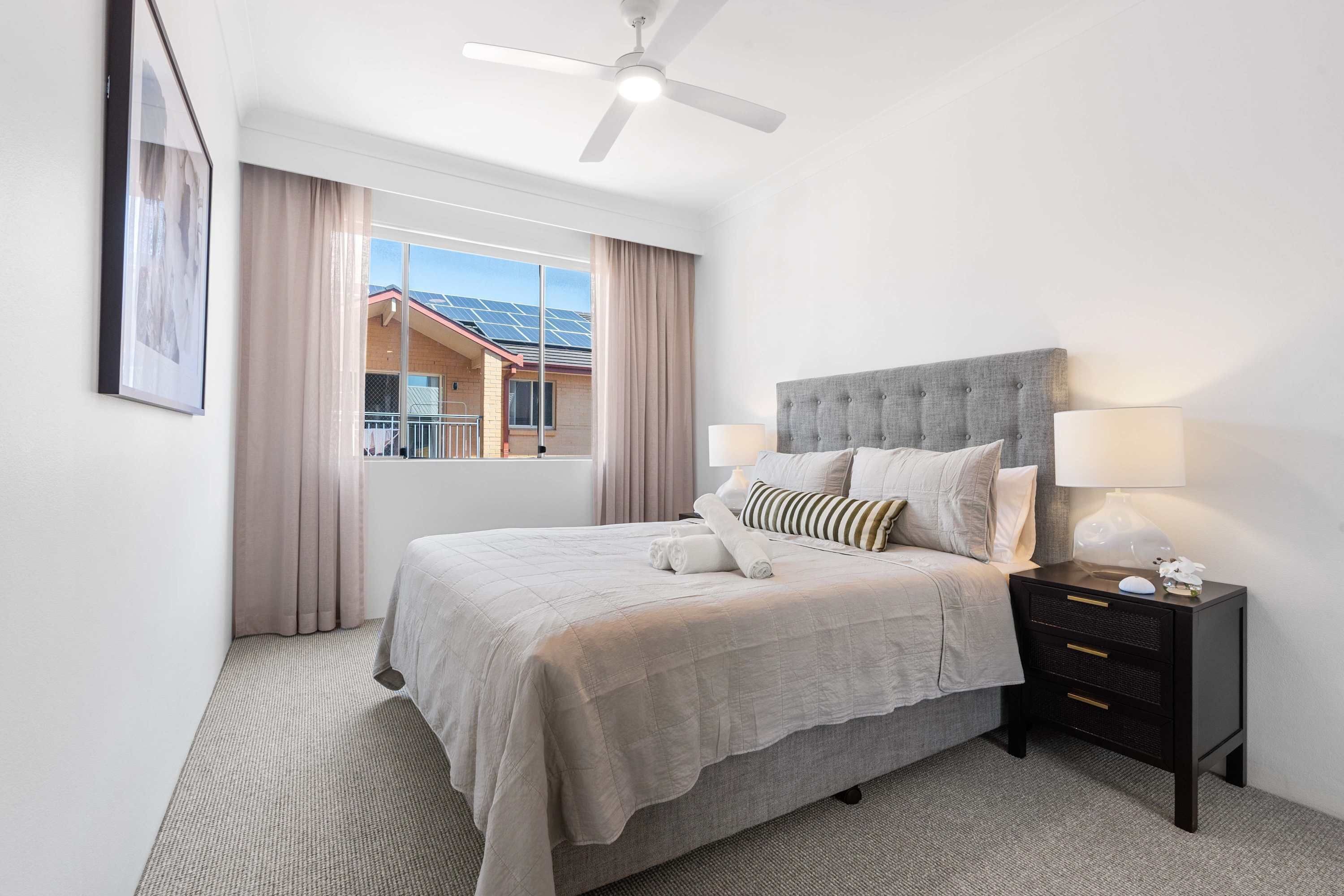 A neatly arranged hotel room with a bed, bedside tables, a ceiling fan, and a window with curtains.