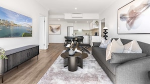 A modern living room with a grey sofa, a coffee table, and a dining area with a black table and chairs. - Camperdown Cozy Corner 10 (Sydney)