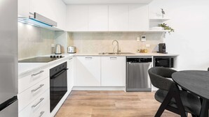 A modern kitchen with white cabinets, a stainless steel dishwasher, and a wooden dining table.