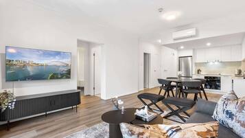 A modern living room with a flat-screen TV, a sofa, a coffee table, and a dining area with a table and chairs.