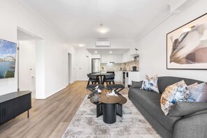A modern living room with a grey sofa, a coffee table, and a dining area with a table and chairs. - Camperdown Cozy Corner 7 (Sydney)