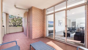Une terrasse couverte avec un banc, un mur en briques et une porte-fenêtre coulissante donnant sur un espace de vie comprenant un canapé et une table.