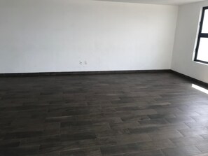 Ein Zimmer mit dunklem Holzboden, weißen Wänden und einem großen Fenster rechts.