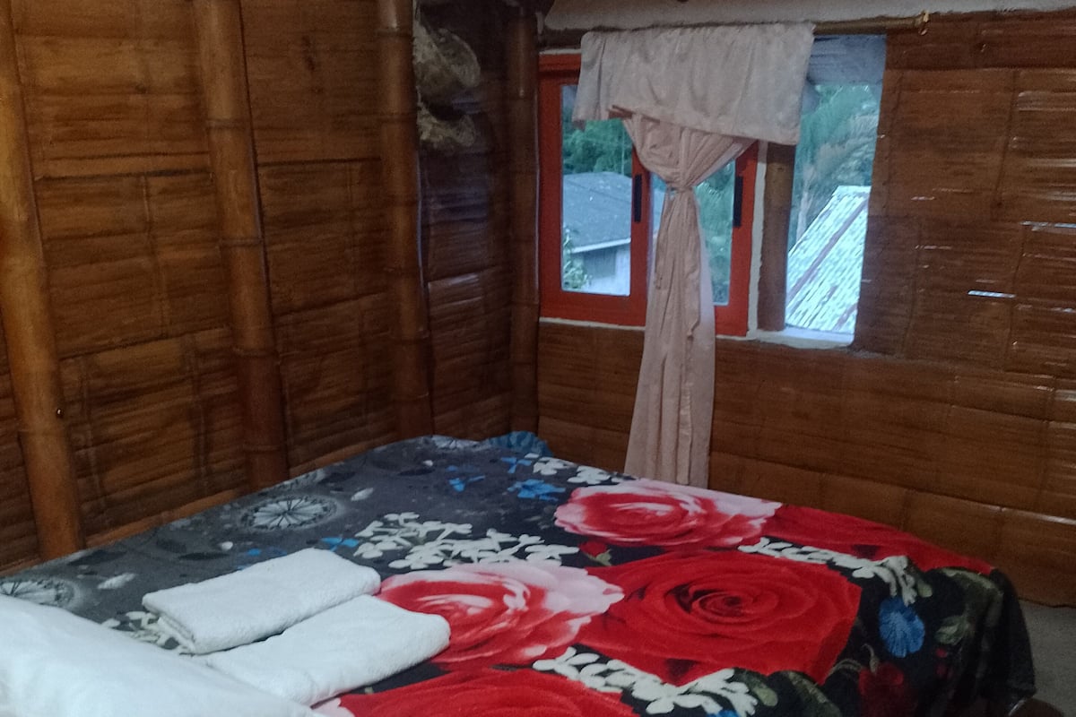 Quarto de madeira com cama, janela com cortina e vista para o exterior.