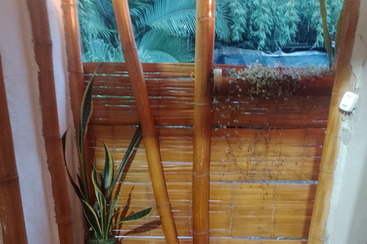 Um corredor estreito com pilares de bambu, piso de azulejos e um vaso de planta.
