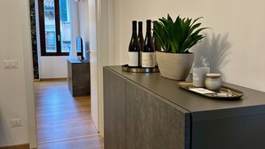 Una moderna zona de recepción de hotel con un mostrador oscuro, botellas de vino, una planta en maceta y una vela.