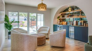 A modern kitchen with a built-in island, a dining area with two chairs, and a large window providing a view of the backyard. - Family & Dog-Friendly Luxury Tudor Home in Richardson, TX w/ Pool and Spa (Richardson)