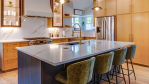 A modern kitchen with a large island, bar stools, wooden cabinets, stainless steel appliances, and pendant lighting. - Family & Dog-Friendly Luxury Tudor Home in Richardson, TX w/ Pool and Spa (Richardson)