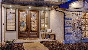 A modern house with a wooden front door, a bench, and a small table outside. - Family & Dog-Friendly Luxury Tudor Home in Richardson, TX w/ Pool and Spa (Richardson)