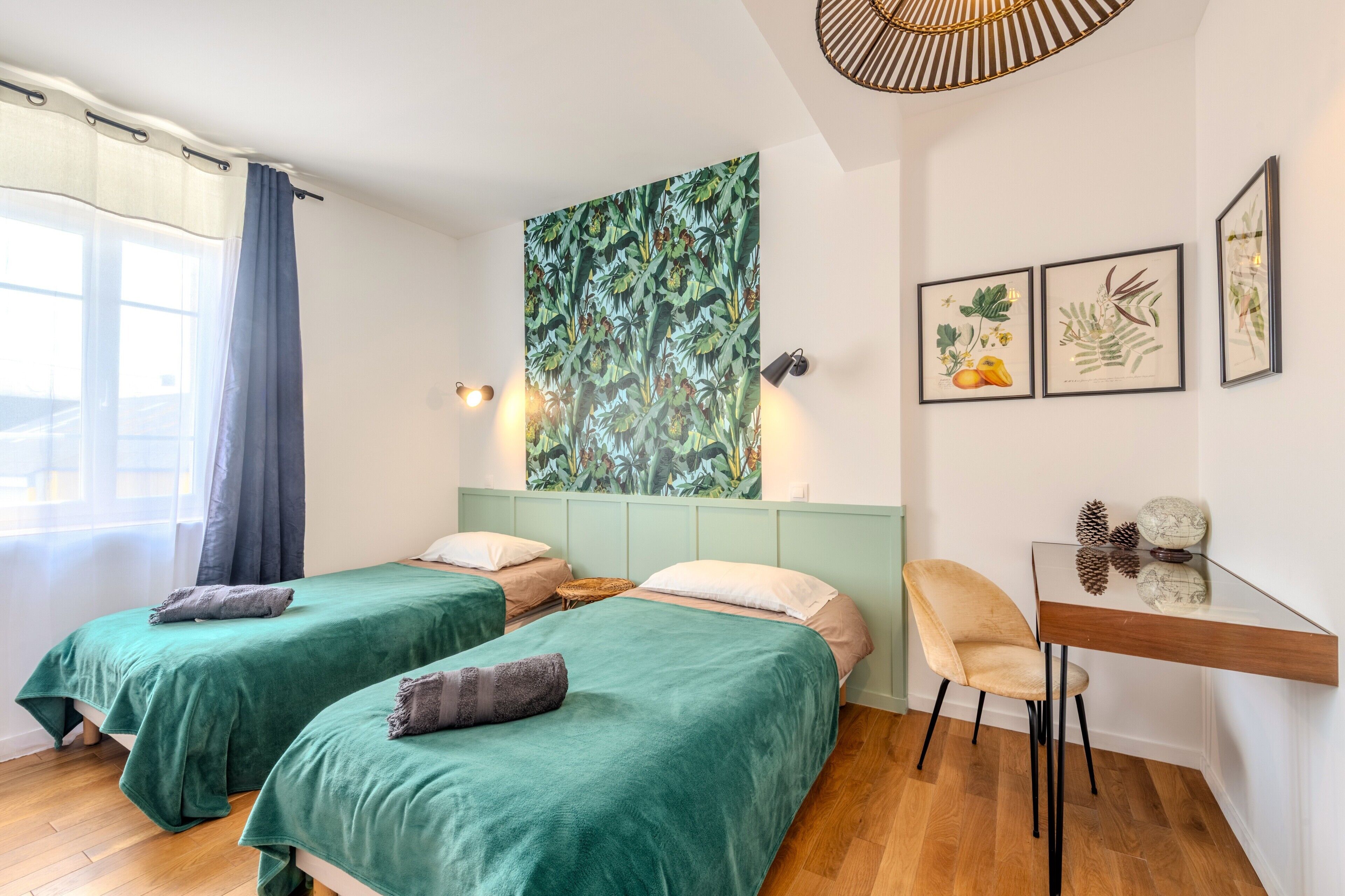 A room with two beds, a desk, and a large botanical print on the wall.