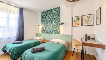 A room with two beds, a desk, and a large botanical print on the wall.