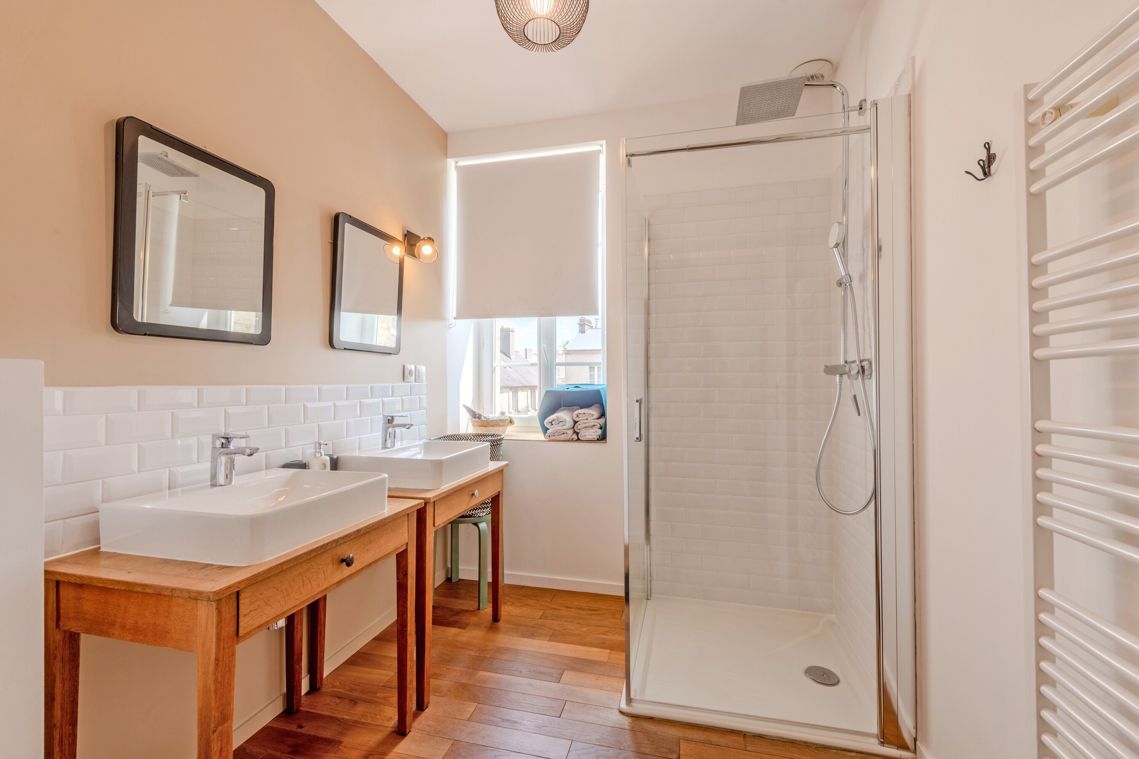 Een badkamer met twee wastafels, een spiegel, een douche en een raam met jaloezieën.