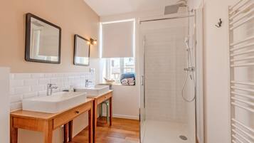 Een badkamer met twee wastafels, een spiegel, een douche en een raam met jaloezieën.