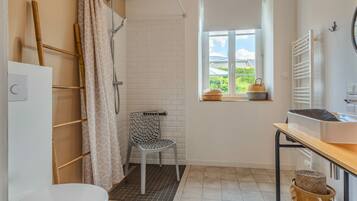 Een badkamer met douche, toilet en een raam met uitzicht.