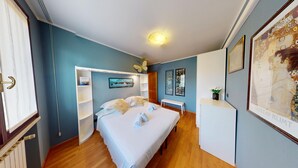 A hotel room with a bed, a desk, a chair, a shelf with a 'BOOKING' sign, and a framed picture on the wall.