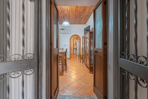 A hallway with wooden doors, a tiled floor, and a dining area with chairs and a table.