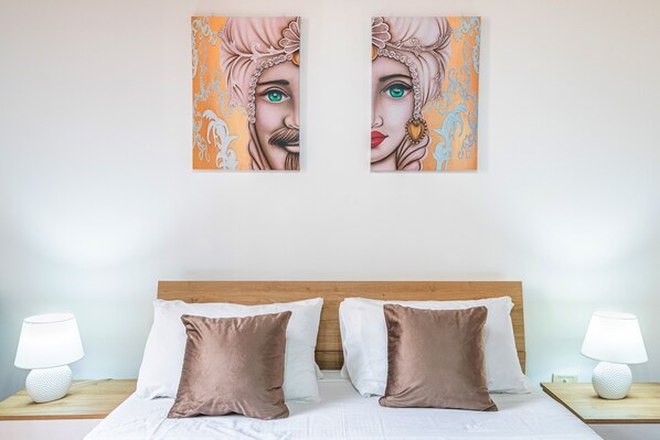 A bed with white and brown pillows, two bedside tables with lamps, and two wall-mounted paintings.