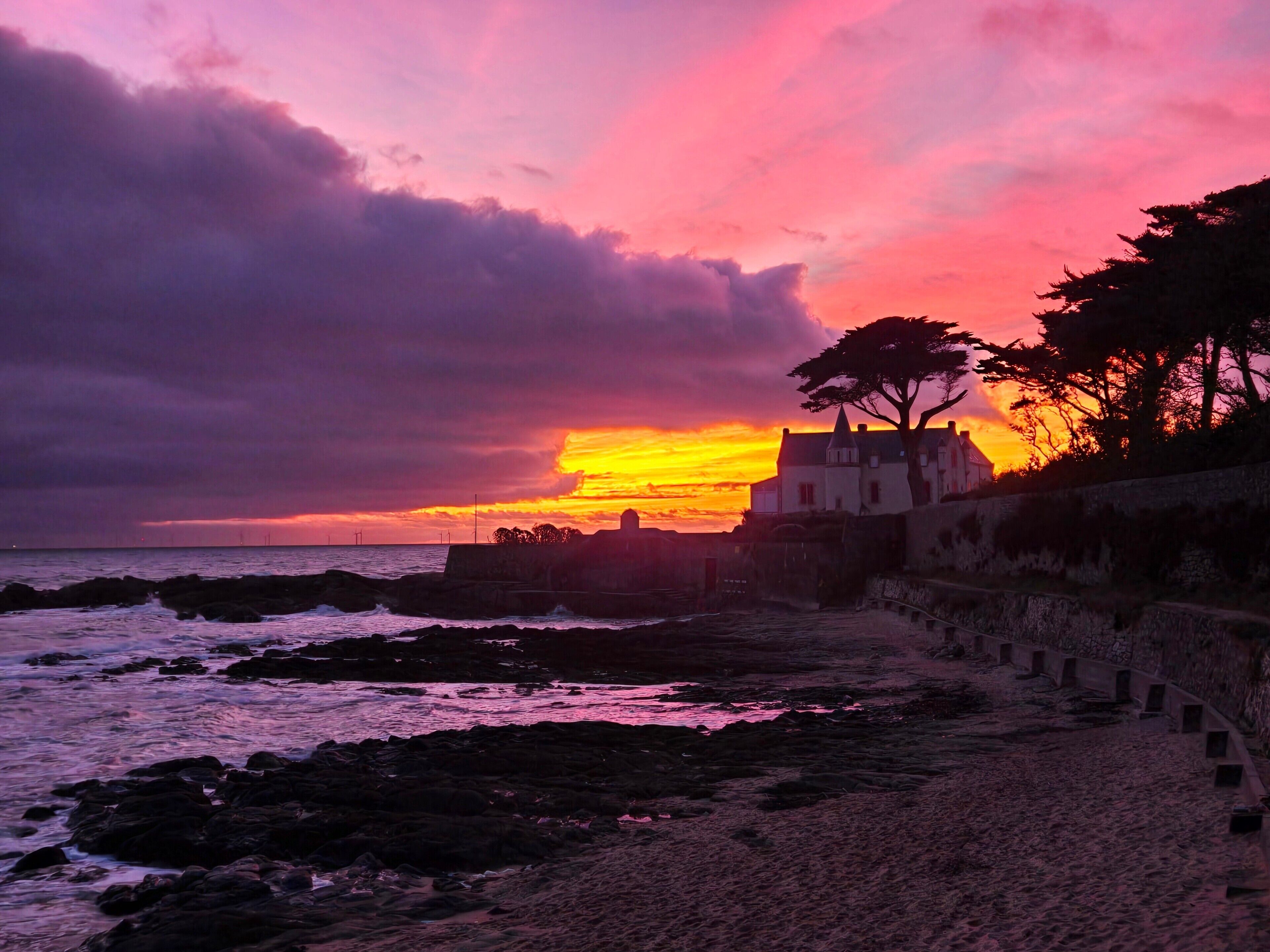 A coastal scene with a building, rocky shoreline, and a sunset.