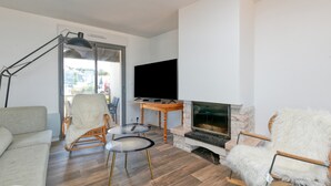 A living room with a sofa, a chair, a table, a TV, and a fireplace. - Villa 'Léa Vue Mer D'exception Plage' with Sea View, Private Terrace and Wi-Fi (Batz-sur-Mer)