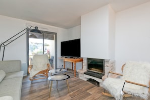Uma sala de estar com sofá, poltrona, mesa, televisão e lareira.