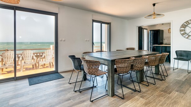 A modern dining area with a large table, wicker chairs, and a view of the ocean through large glass doors. - Villa 'Léa Vue Mer D'exception Plage' with Sea View, Private Terrace and Wi-Fi (Batz-sur-Mer)