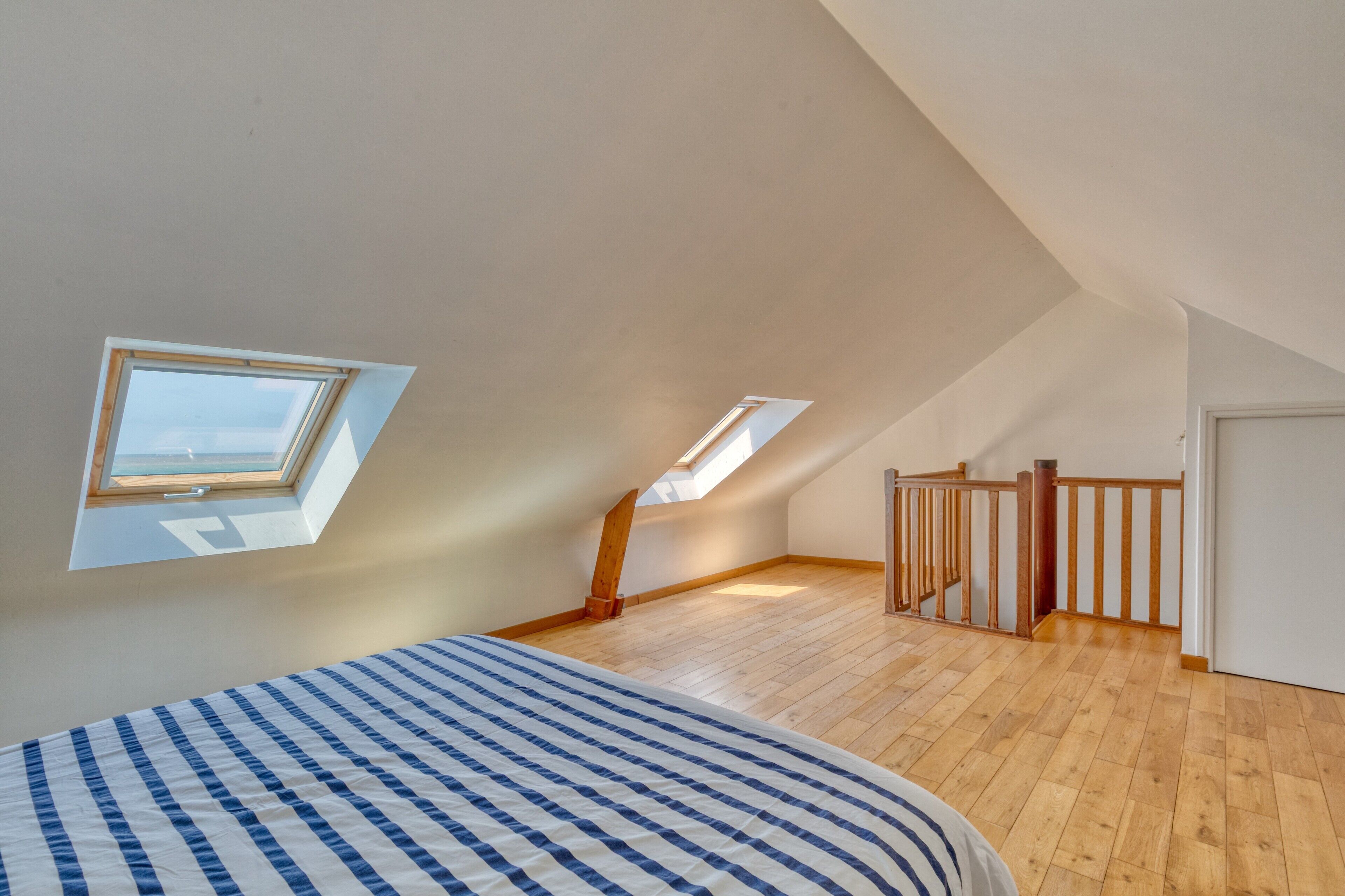A bedroom with a sloped ceiling, skylights, a wooden floor, and a bed with a striped bedspread.