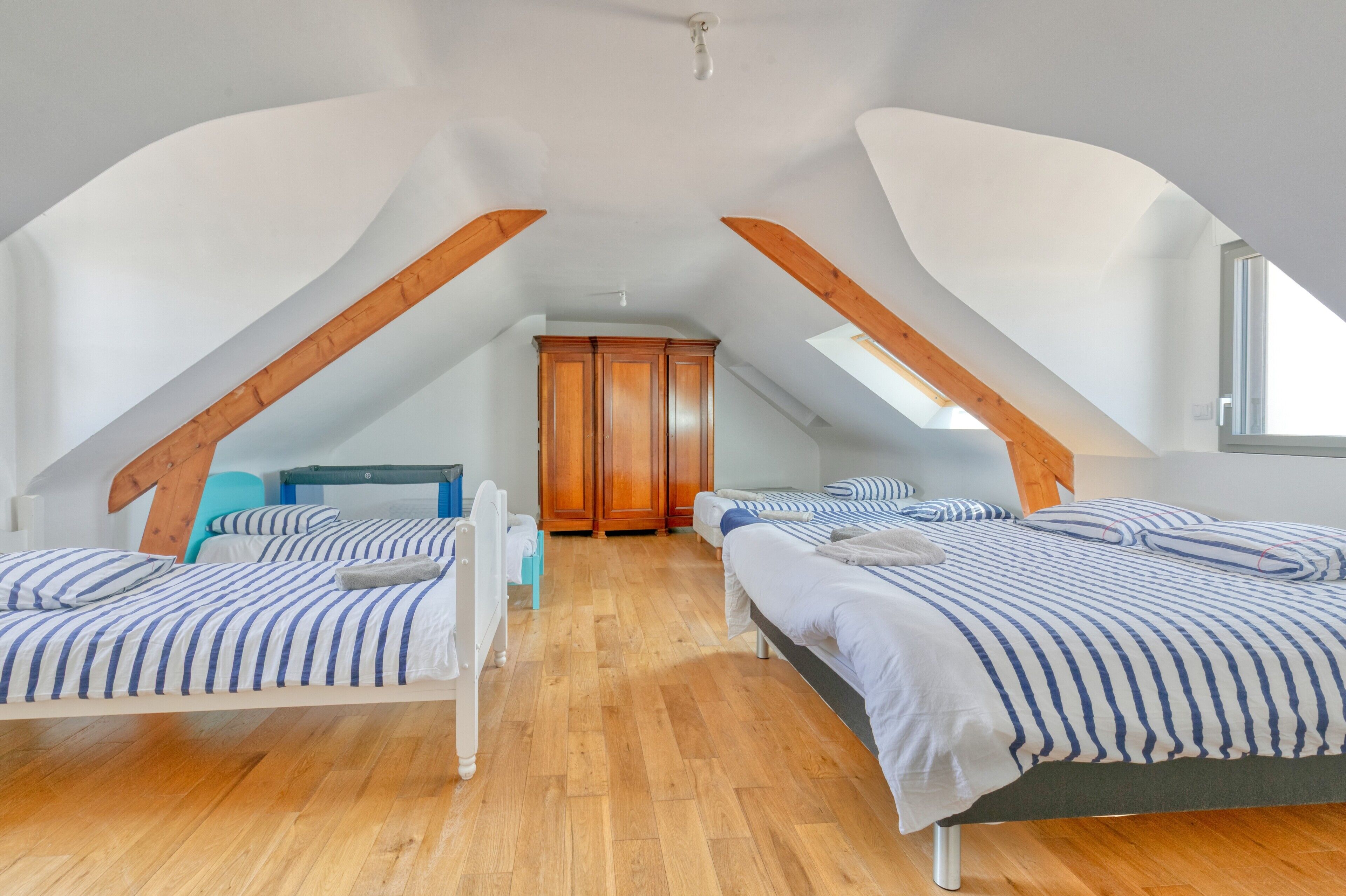 Un dormitorio con dos camas, vigas de madera, un armario y un tragaluz.