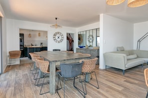 Cozinha moderna com uma ilha grande, sala de jantar com cadeiras de vime e um sofá em um espaço de estar iluminado.