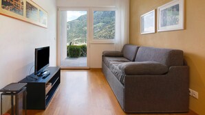 Una sala de estar con un sofá, un televisor sobre un mueble bajo y un ventanal con vista a la montaña.