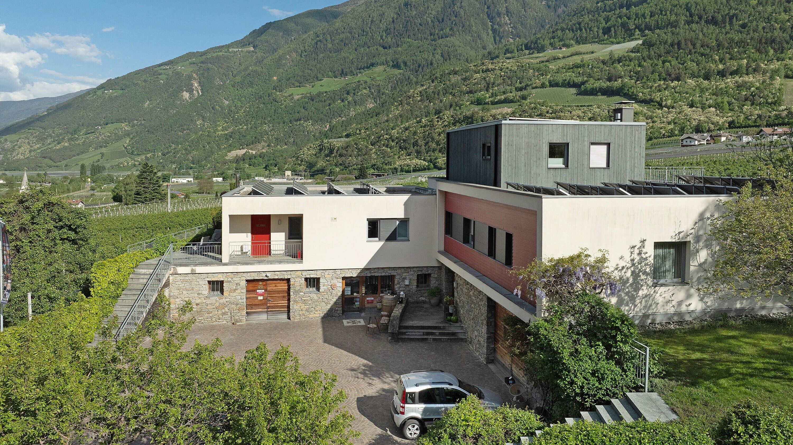 Un bâtiment moderne, doté d’un socle en pierre et d’un toit plat, entouré de verdure et surplombé par un paysage montagneux.