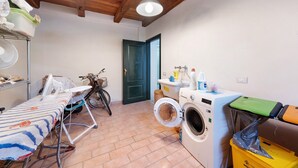 A laundry room with a washing machine, ironing board, and bicycle.