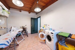 A laundry room with a washing machine, ironing board, and bicycle.