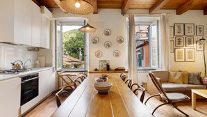 A dining area with a wooden table, chairs, a kitchen with white cabinets, and a view of the outdoors.