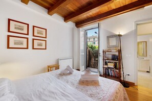 Un dormitorio con una cama grande, techo de madera, radiador, estantería y una puerta que da a un balcón.