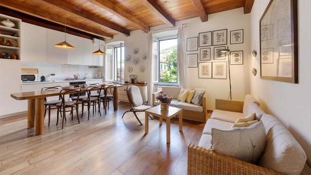 A spacious living area with a wooden dining table, chairs, a sofa, and a kitchen in the background.