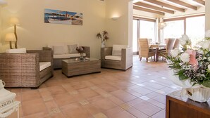 A spacious living area with wicker furniture, a coffee table, and a dining area with chairs and a table. - Holiday Home 'Pescadores' with Sea View, Private Terrace and Air Conditioning (Son Moll)
