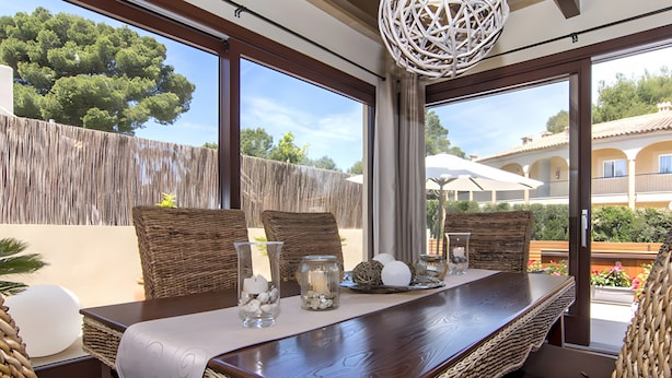 A dining area with a table set for two, wicker chairs, and a view of the outdoors. - Holiday Home 'Pescadores' with Sea View, Private Terrace and Air Conditioning (Son Moll)