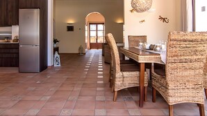 A spacious kitchen with a built-in refrigerator, a dining area with wicker chairs and a wooden table, and a view of a dining room through an archway. - Holiday Home 'Pescadores' with Sea View, Private Terrace and Air Conditioning (Son Moll)