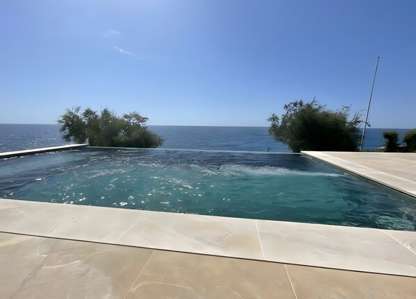 Una piscina con vistas al mar, rodeada de árboles y un cielo despejado.
