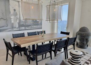 Un comedor moderno con una mesa de madera, sillas negras, una estatua de Buda y un amplio ventanal con vistas.